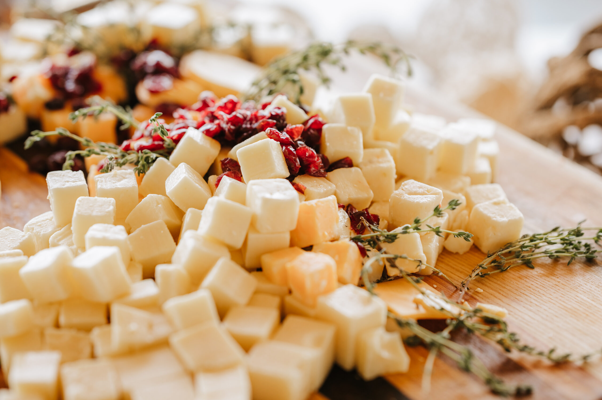 Assorted Cheese Board with Fresh Herbs Close-up shot of cubed cheeses from a cheese board, garnished with fresh sprigs of thyme, showcasing a delicious and elegant appetizer option for weddings and events.