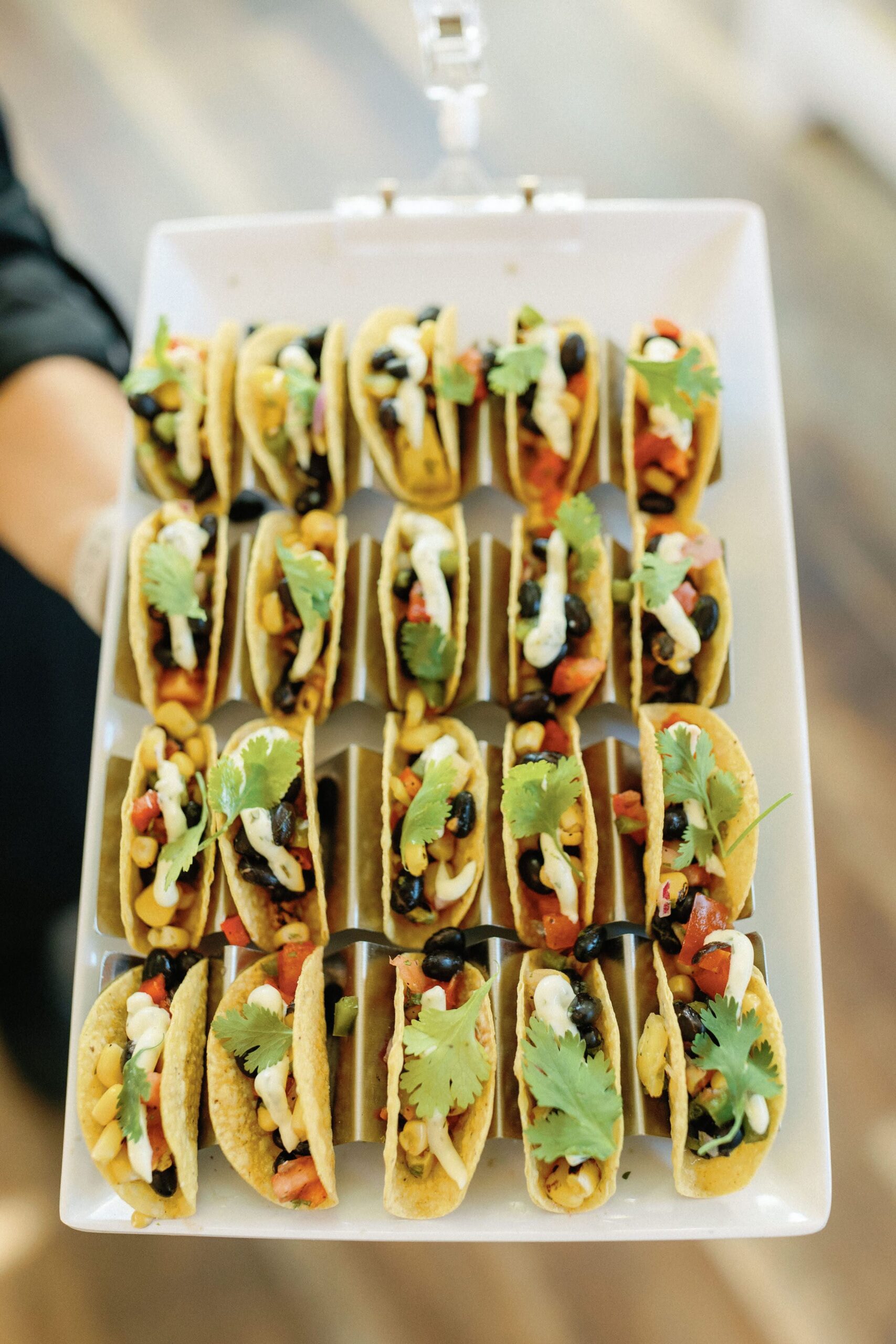 Miniature Hand-passed Vegetarian Tacos Hand-passed platter of miniature vegetarian tacos served in hard shells, filled with black beans, charred corn, cilantro, and topped with lime aioli, perfect for weddings and events.