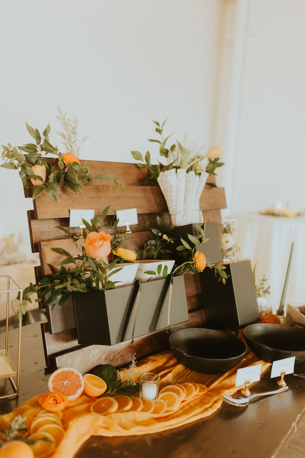 Asian Noodle Bar Station Display A decorative Asian Fusion Station display featuring black containers holding chopsticks and toppings, accented with orange roses and greenery. Sliced citrus, candles, and bowls rest on an orange fabric runner for a vibrant presentation.