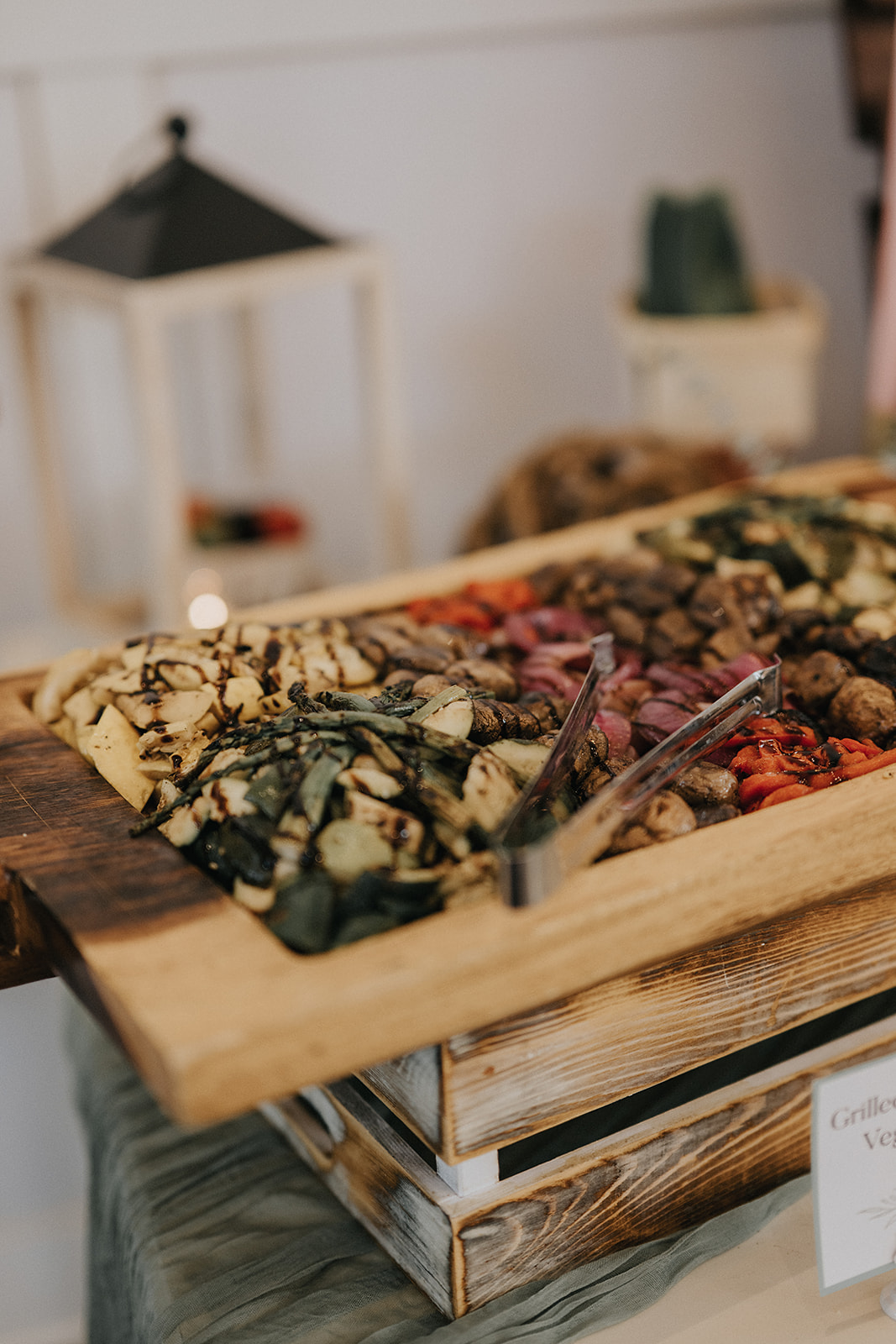 Grilled and Chilled Vegetable Display Grilled and Chilled Vegetable Display in a wooden serving dish on a table with signage and a eucalyptus green table runner. Lanterns and vine balls accent the table in the background.