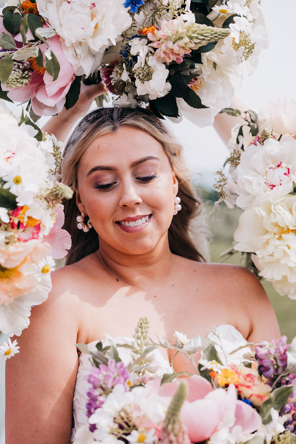 Bride Among Blooms Bride surrounded by lush bouquets of white, pink, and colorful flowers, smiling with eyes closed.