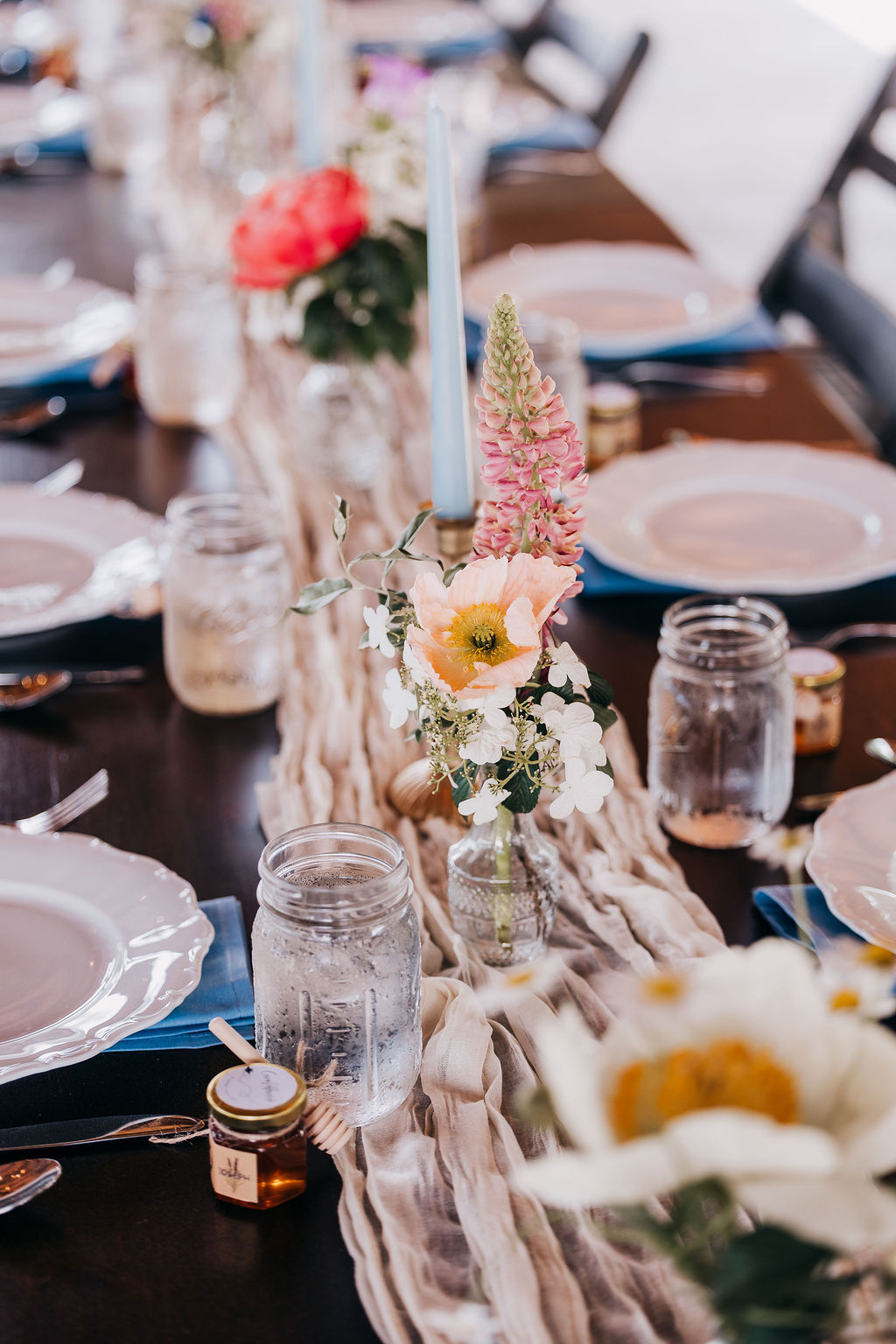 Elegant Reception Table Décor Wedding reception table decorated with floral centerpieces, blue candles, mason jar glasses, and place settings.