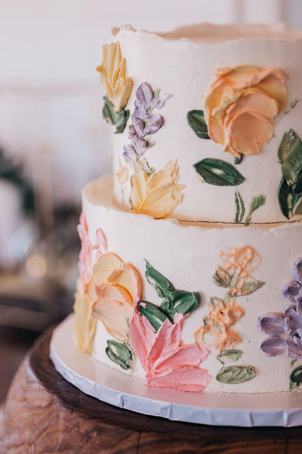 Floral Wedding Cake Close-up of two-tiered wedding cake with painted buttercream flowers in pastel colors.