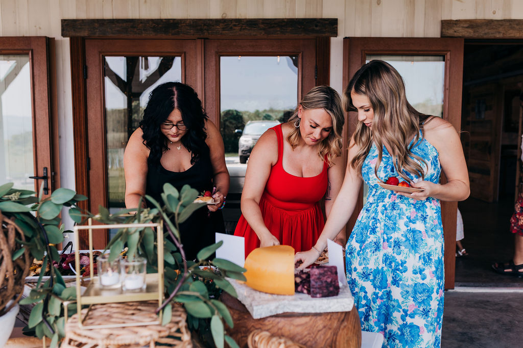 Guests Enjoying the Appetizer Table Three women in colorful dresses serving themselves from a cheese and fruit display at a wedding reception.