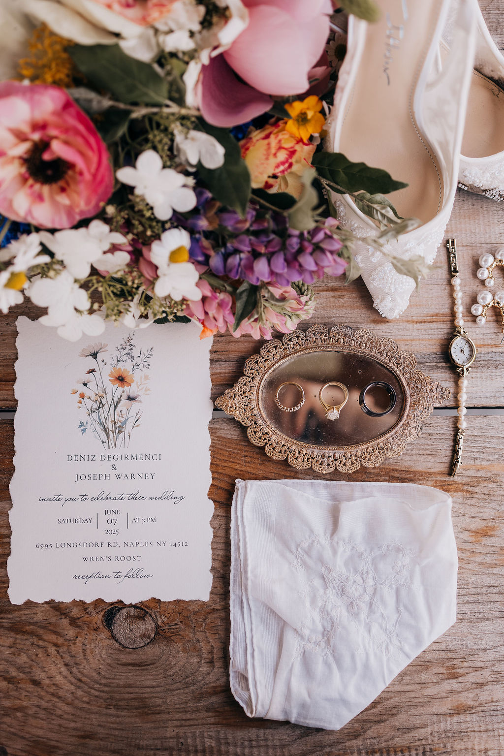 Wedding Invitation Flatlay Wedding invitation with floral design styled alongside rings, jewelry, lace handkerchief, and bouquet.