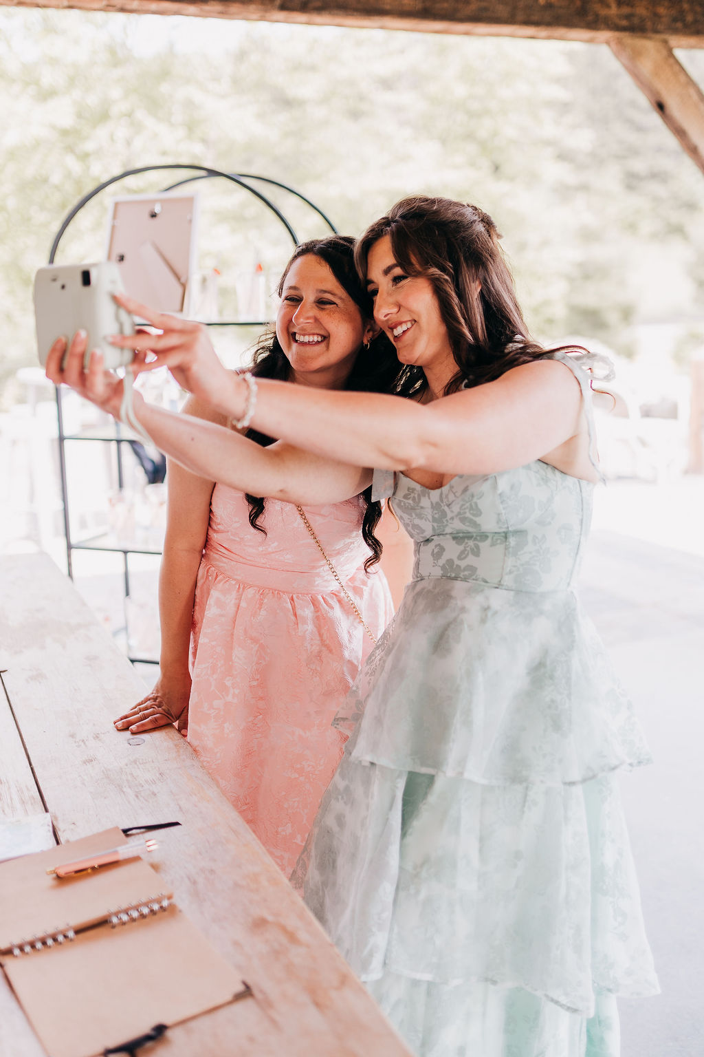 Wedding guest candid Two wedding guests in pastel dresses smiling and taking a selfie during cocktail hour.