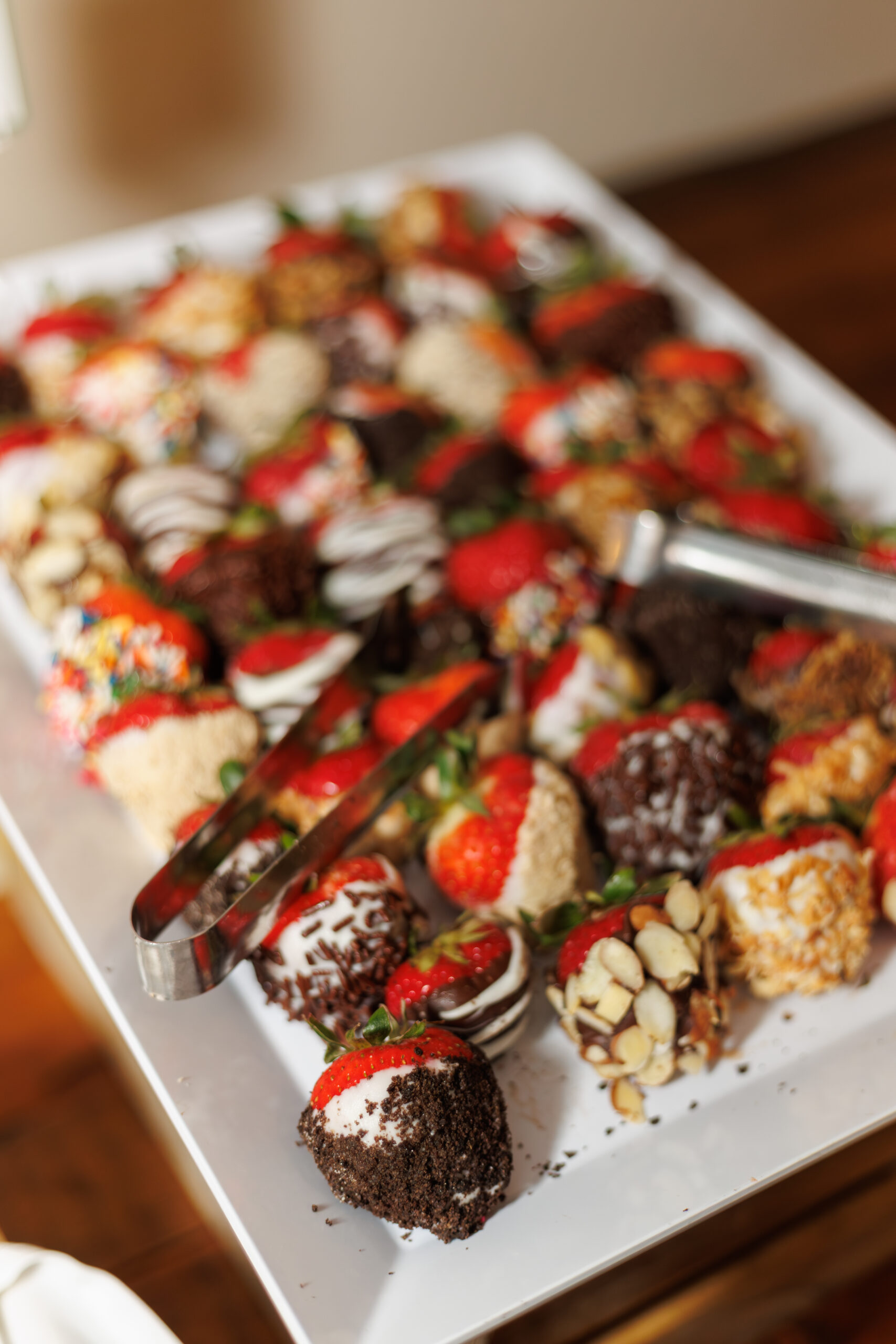 A tray of chocolate-dipped strawberries decorated with almonds, sprinkles, cookie crumbs, and assorted toppings, offering a colorful and sweet dessert option.