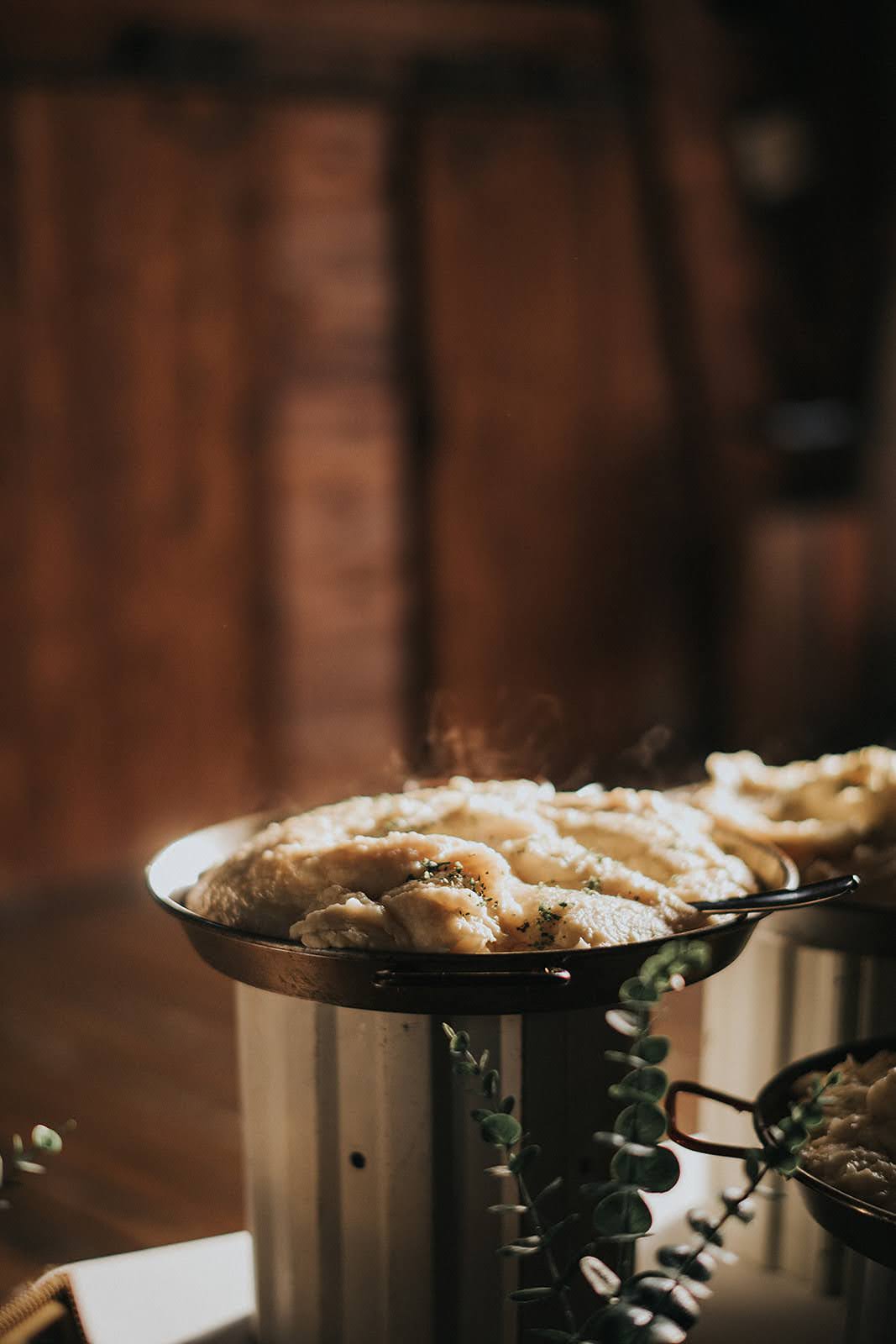 Gourmet Garlic Mashed Potatoes Served Fresh Steaming pans of creamy garlic mashed potatoes garnished with herbs at a buffet station.