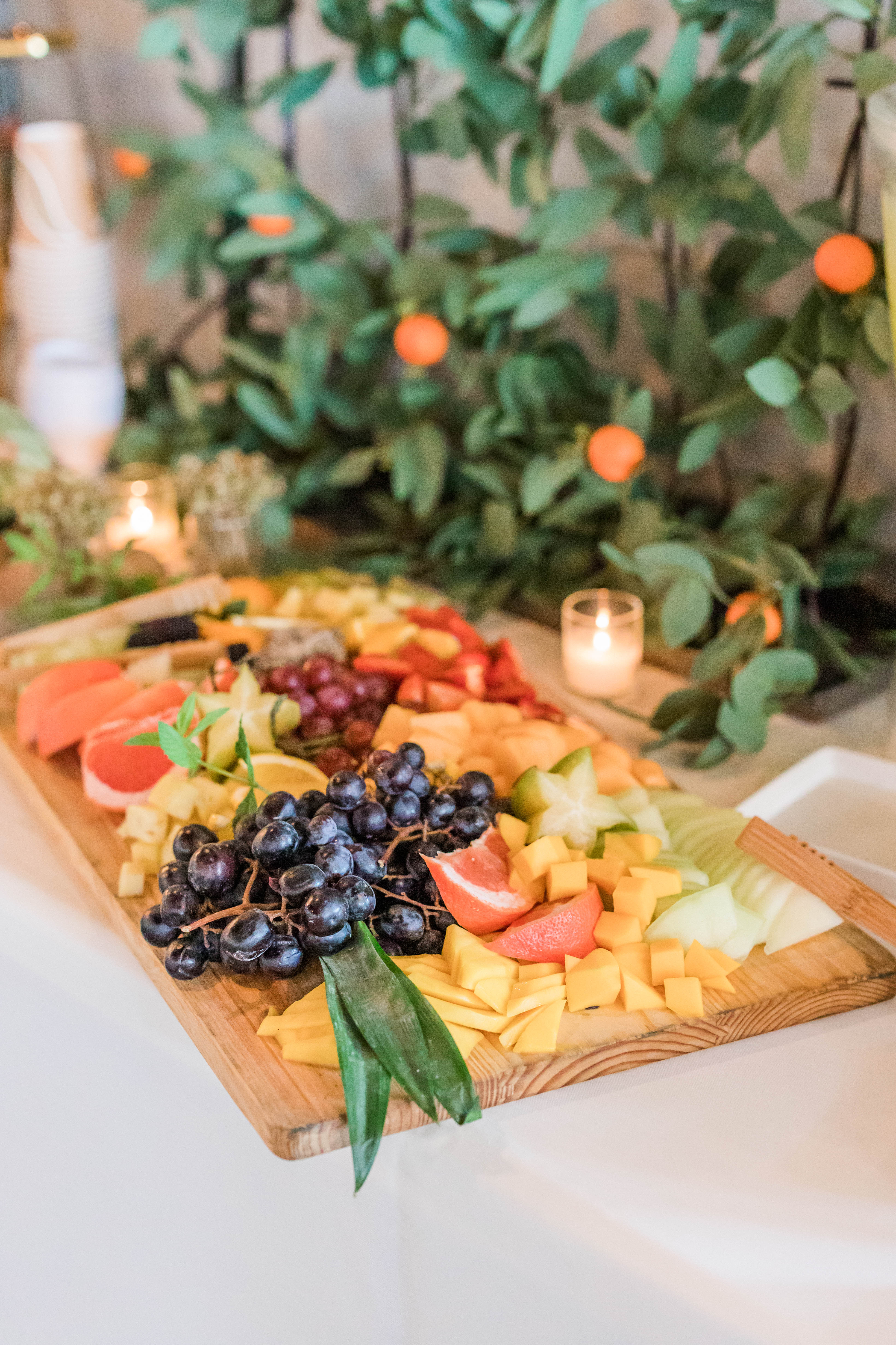 Beautifully styled fruit and cheese board with grapes, melon, citrus, and cubed cheeses on a wooden platter, set for a social event display.