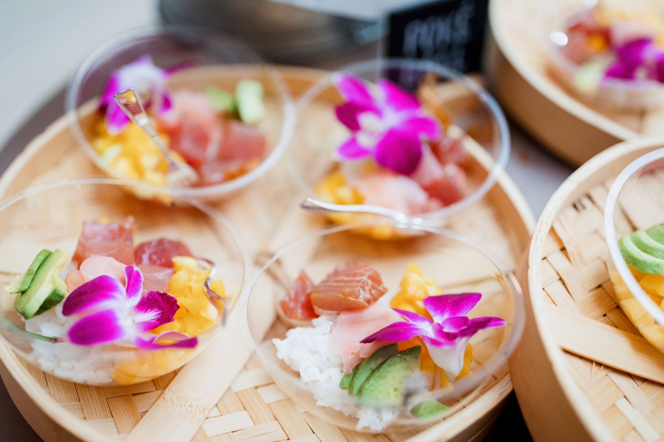 Elegant sushi-style wedding appetizers served in individual cups with fresh fish, avocado, rice, and vibrant edible flowers, showcasing creative and upscale catering presentation.