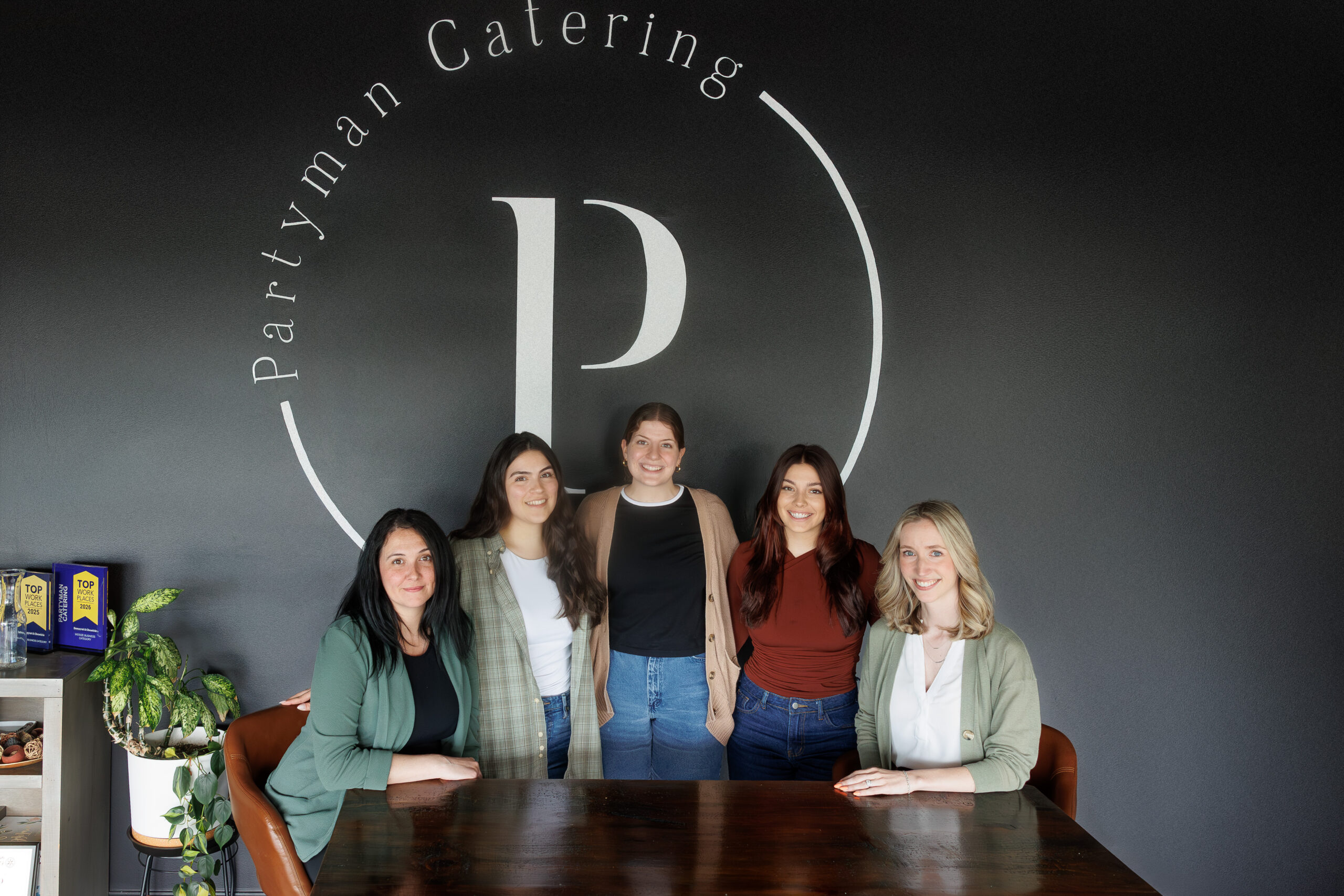Partyman Catering Event Planning team standing together in front of company logo wall in Rochester New York.