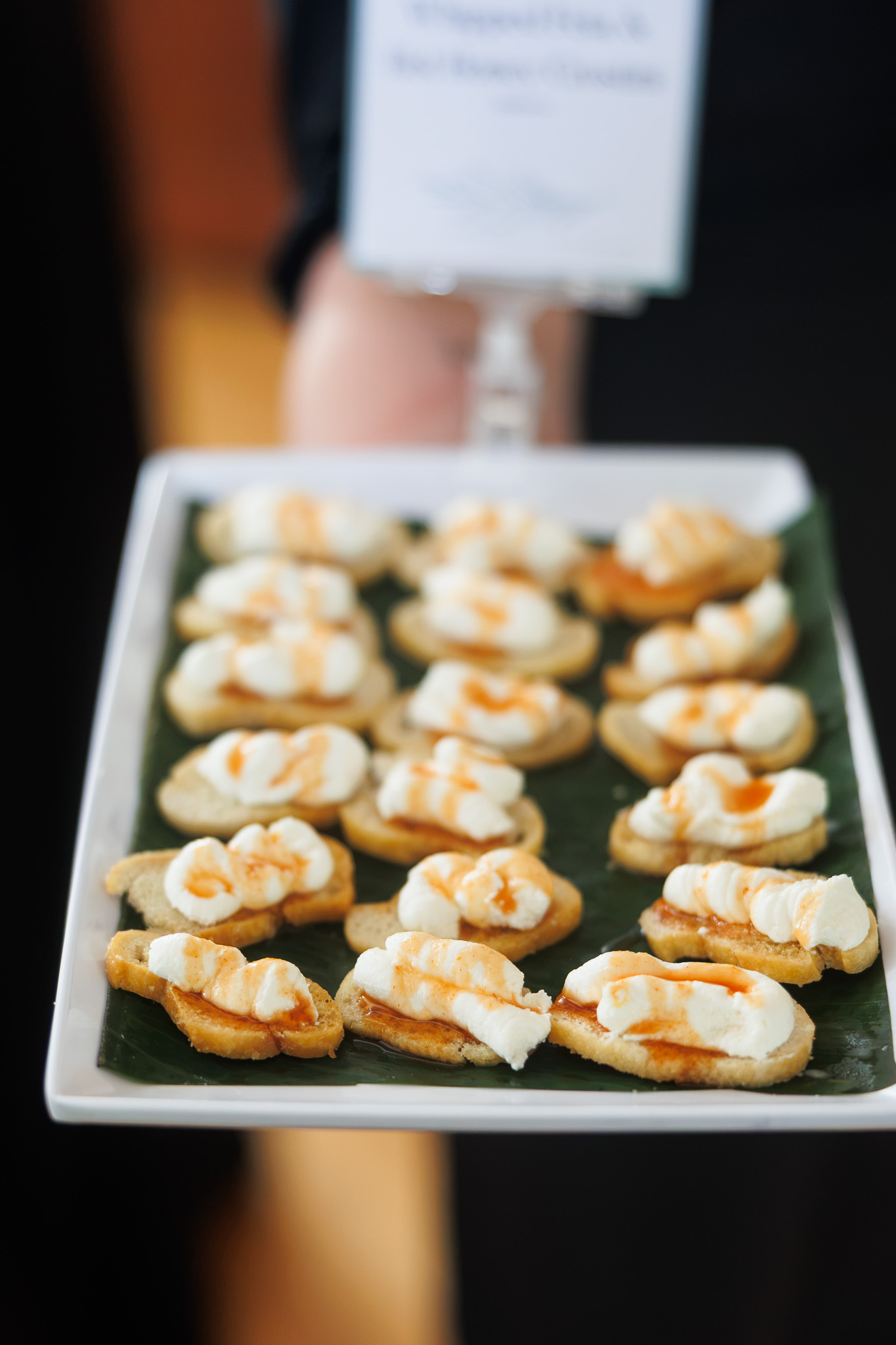 A Partyman Catering team member prepares a grazing and appetizer station before guests arrive at the Historic German House in Rochester. A server presents passed crostini appetizers topped with whipped cheese and hot honey during a catered event by Partyman Catering.