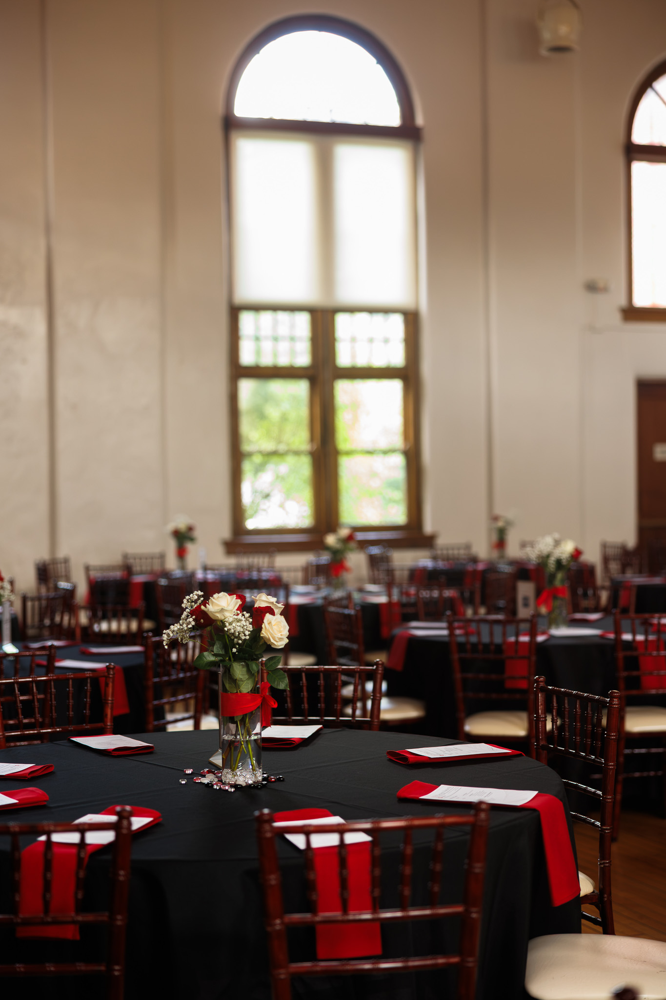 Historic German House Ballroom Setup for Corporate Events | Rochester NY Event Venue Round banquet tables with black linens, red runners, and floral centerpieces arranged inside the Historic German House ballroom for a corporate event.