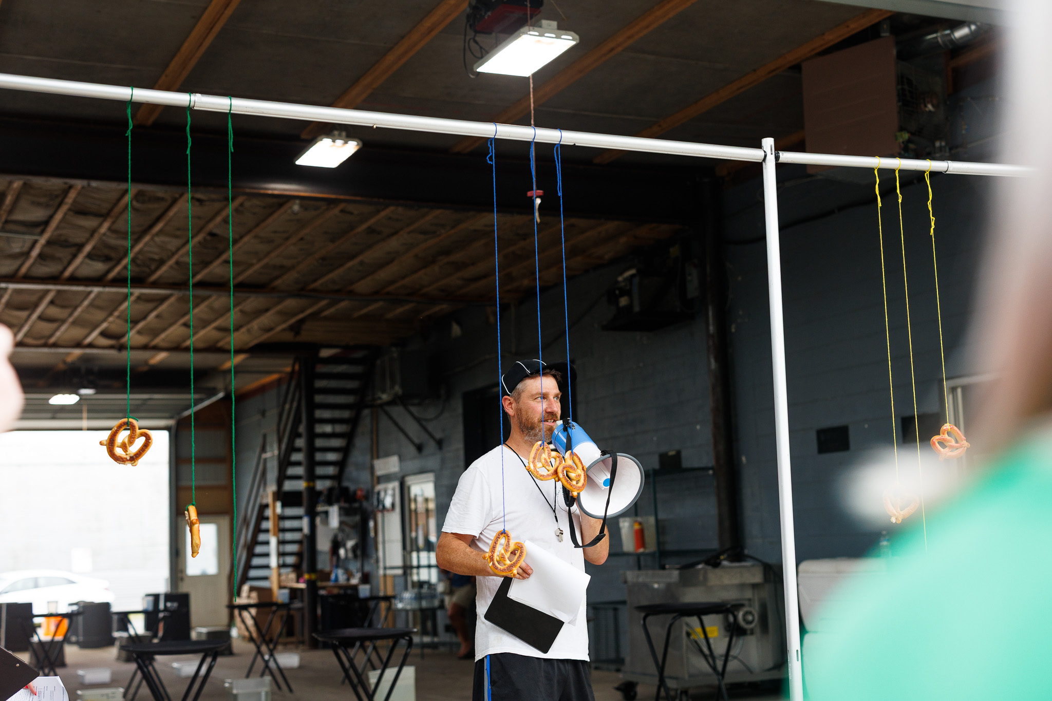 Funner Olympics Pretzel Challenge at Partyman Catering Partyman team member uses a megaphone beside hanging pretzels while leading a playful team-building challenge during the Funner Olympics.