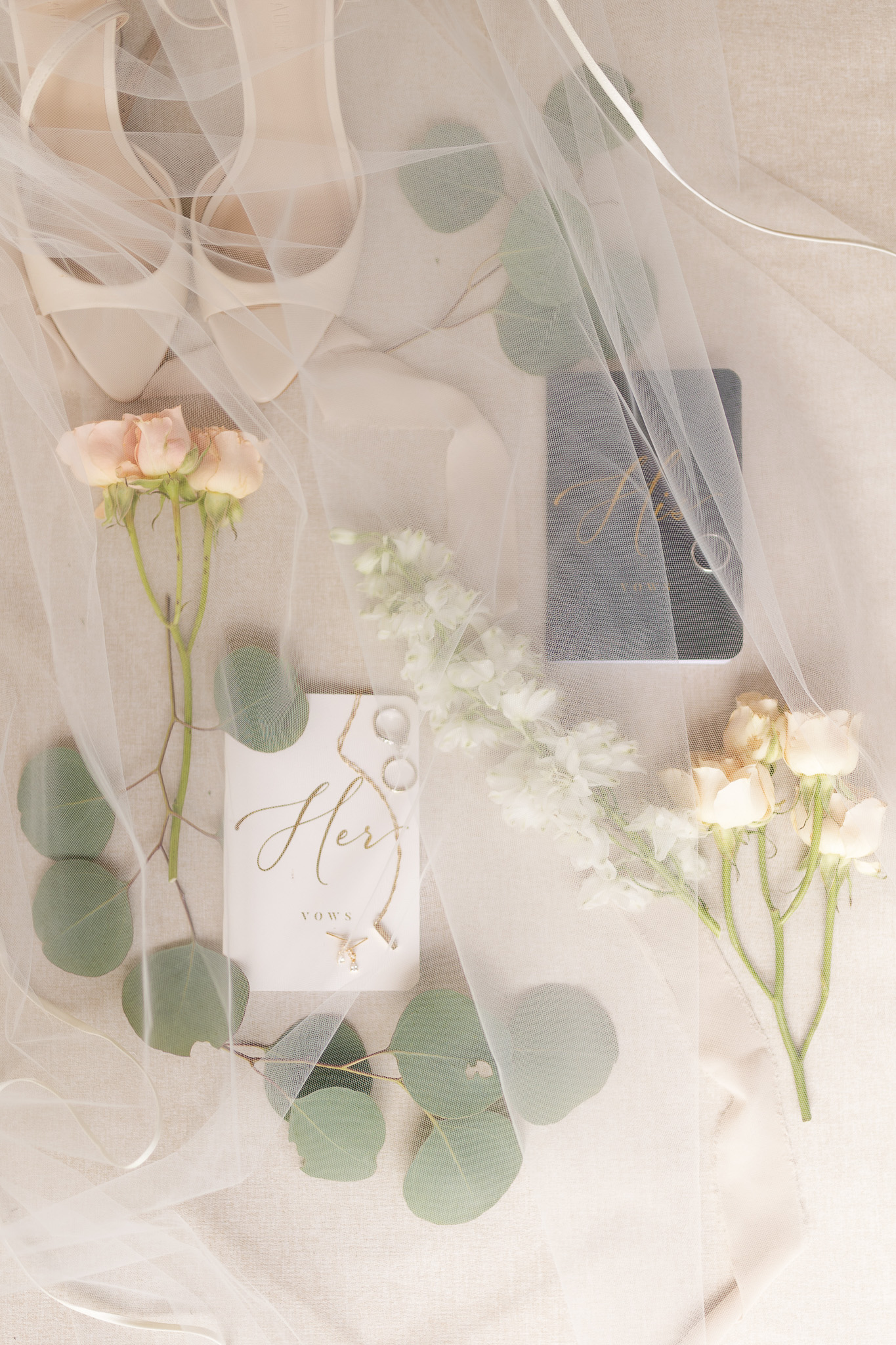 Bridal Details Flat Lay with Veil and Vow Books Romantic bridal detail flat lay featuring a wedding veil, vow books, rings, eucalyptus and soft blush and white flowers.