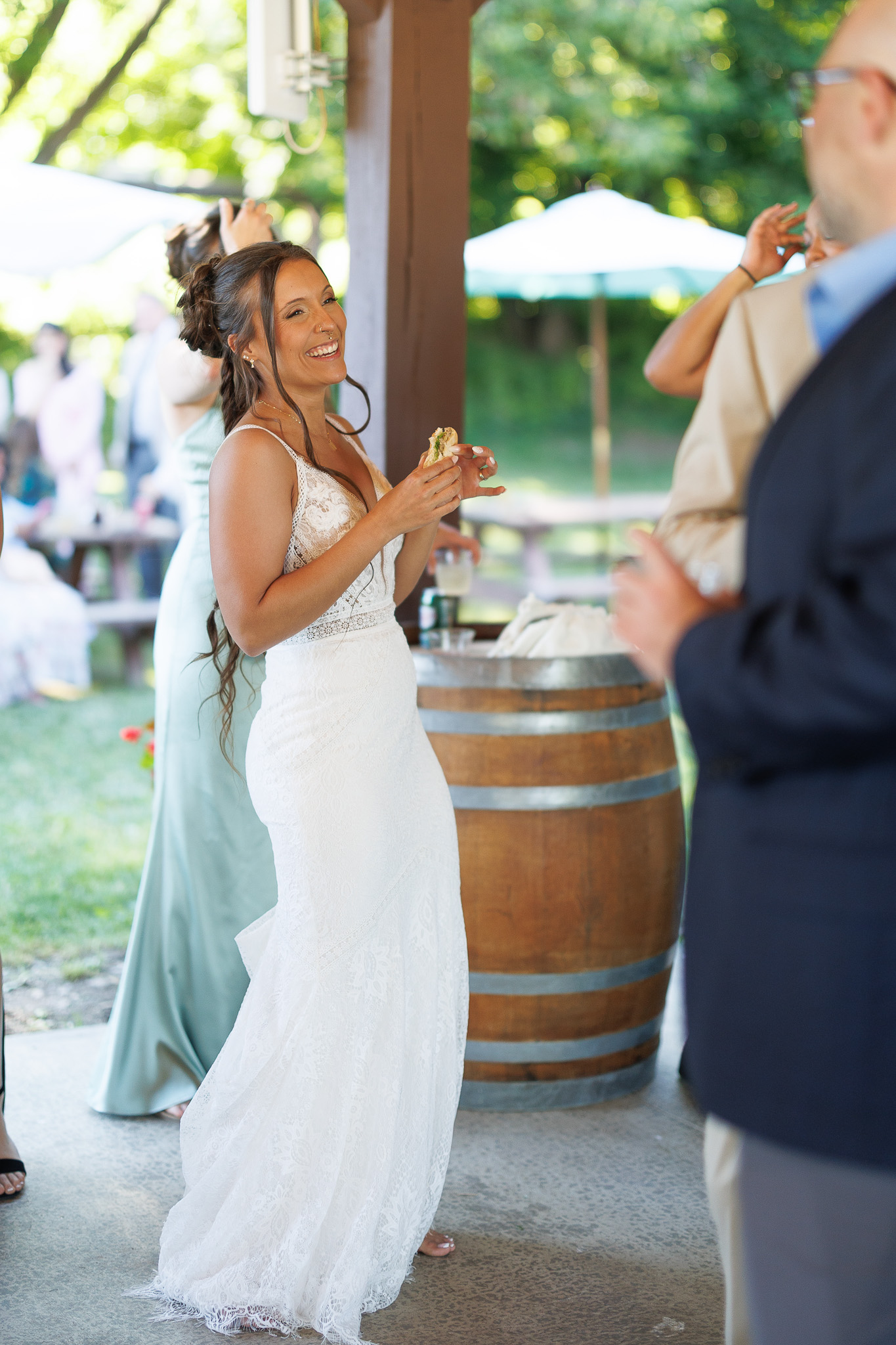 Bride Enjoying Wedding Cocktail Hour Bride in a lace wedding gown smiling while enjoying an appetizer with guests during an outdoor wedding cocktail hour.