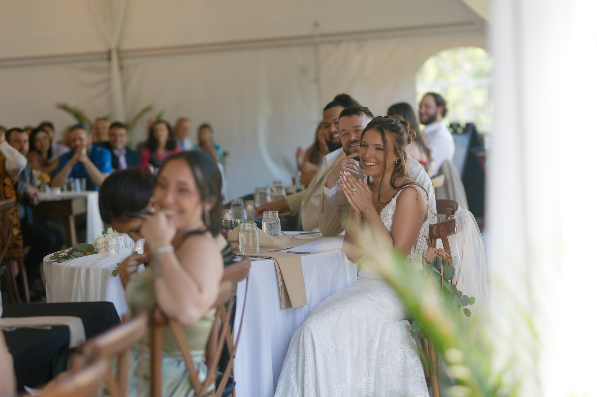Bride & Groom Reception Moment | Inspire Moore Winery Wedding Candid photo of a smiling bride and groom seated together during their wedding reception at Inspire Moore Winery & Vineyard as guests applaud around them.