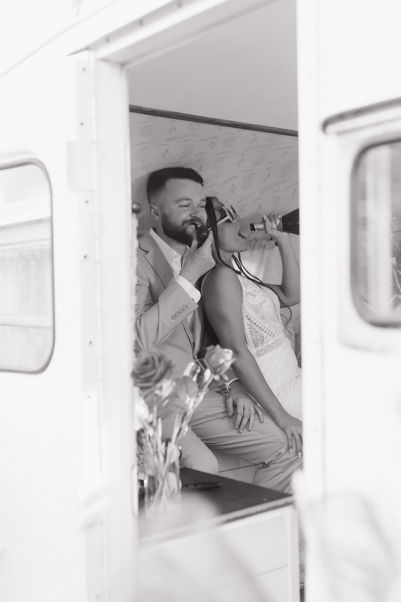 Candid Wedding Photo Booth Moment | Inspire Moore Winery Black-and-white candid photo of a newlywed couple sharing a playful drink inside a vintage photo booth during their wedding at Inspire Moore Winery & Vineyard.