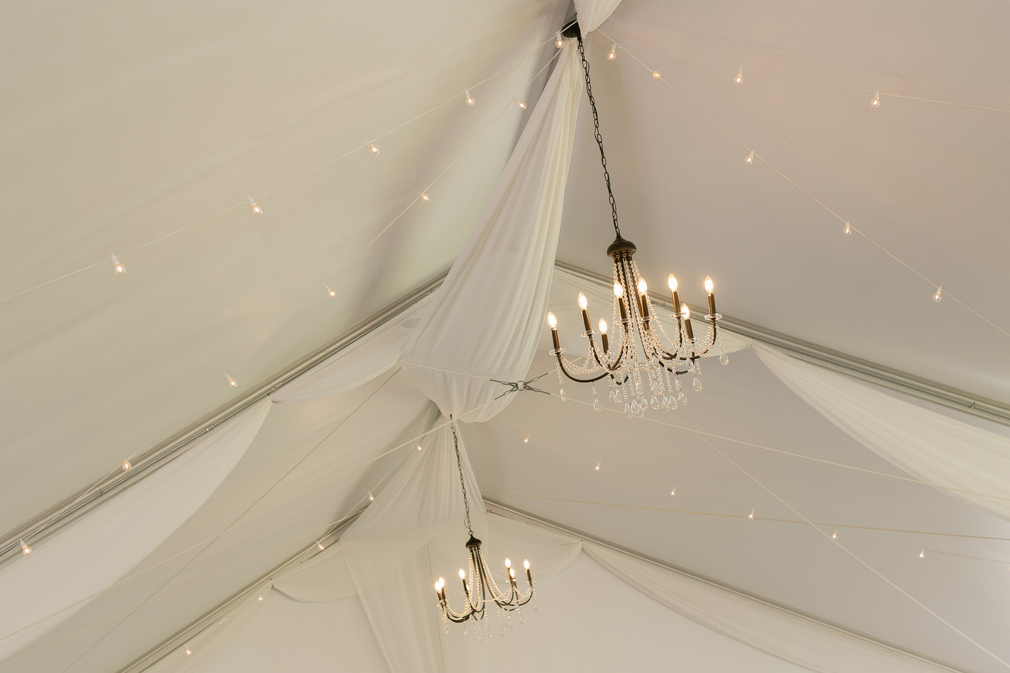 Elegant Wedding Reception Draping and Crystal Chandeliers White ceiling draping, crystal chandeliers, and warm string lights create an elegant wedding reception setting.
