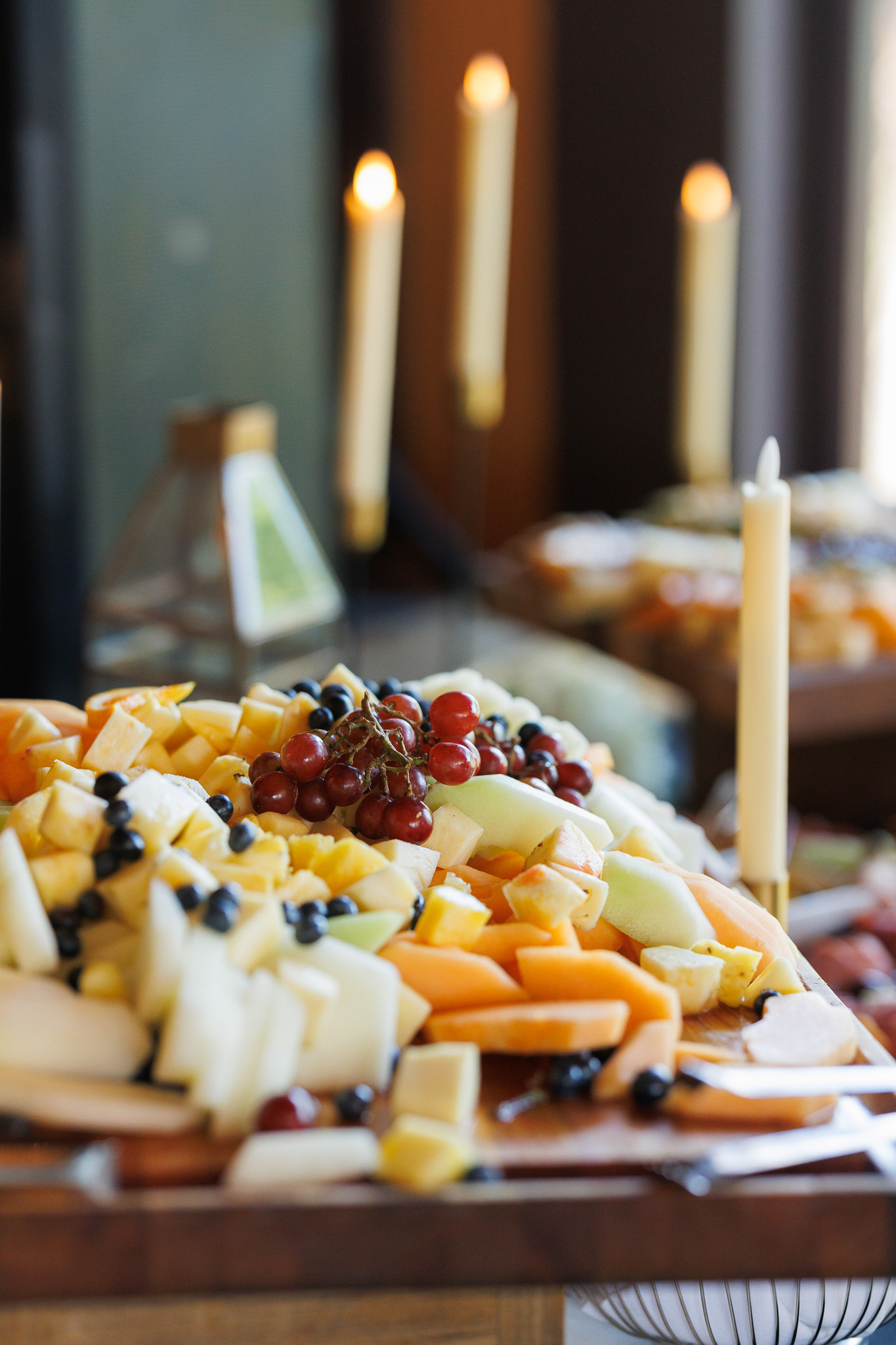 Fresh Fruit Display for Wedding Cocktail Hour Close-up of a colorful fresh fruit display with melon, pineapple, grapes and blueberries arranged on a wooden serving board.