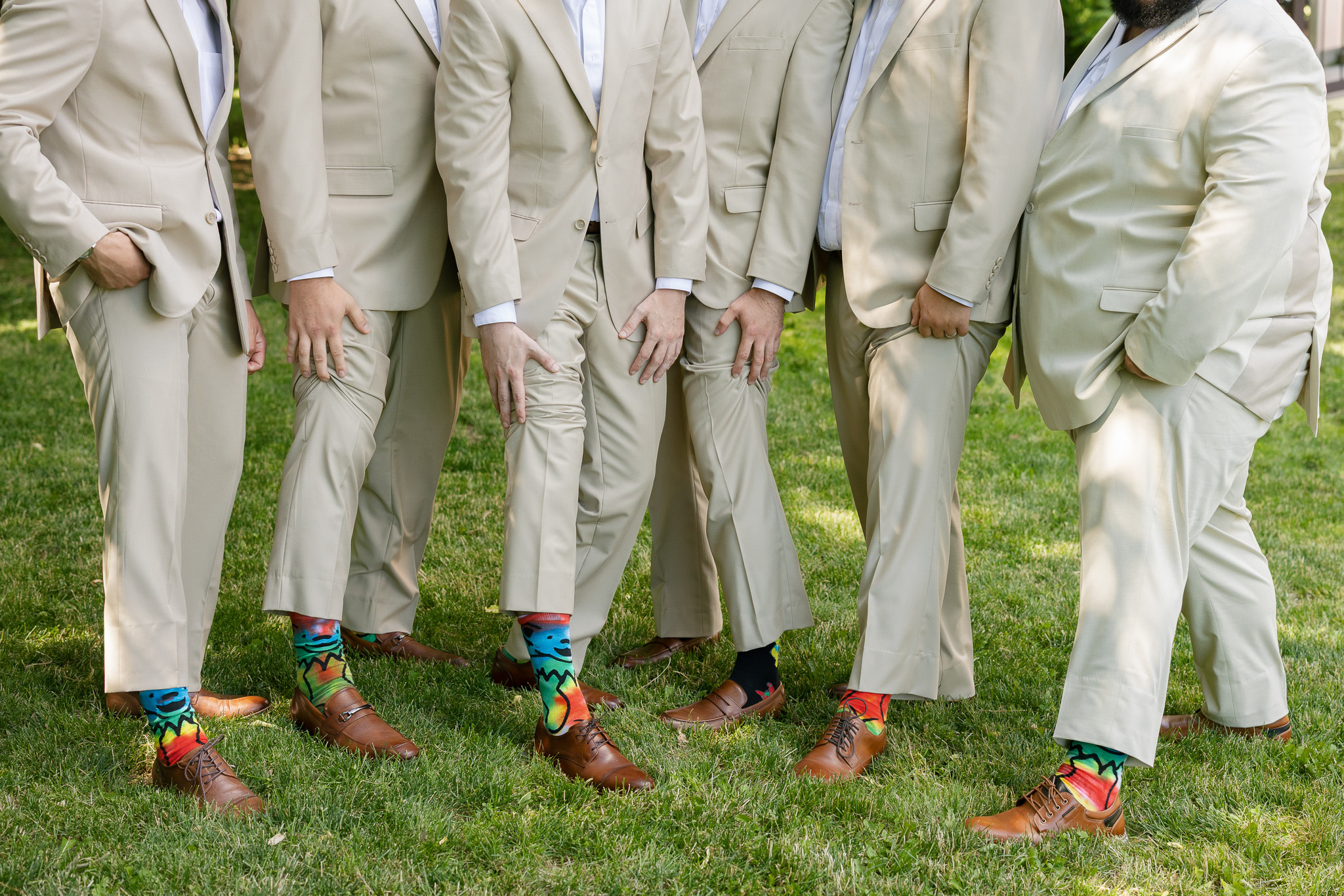 Groomsmen Colorful Wedding Socks Detail Groomsmen in matching light neutral suits showing off colorful patterned socks with brown dress shoes during wedding portraits.