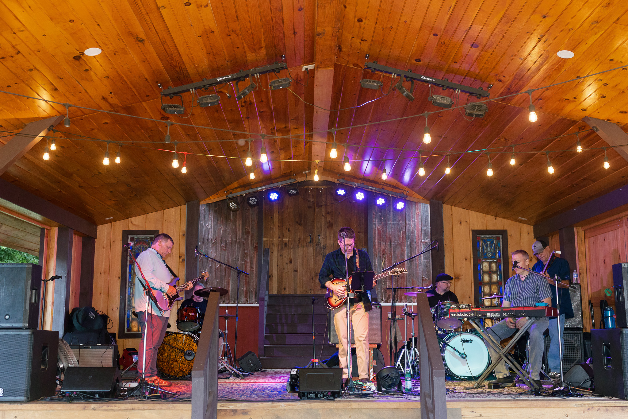 Live Wedding Band at Winery Reception | Inspire Moore Winery Live wedding band performing on a rustic wooden stage beneath warm string lights during a reception at Inspire Moore Winery & Vineyard.