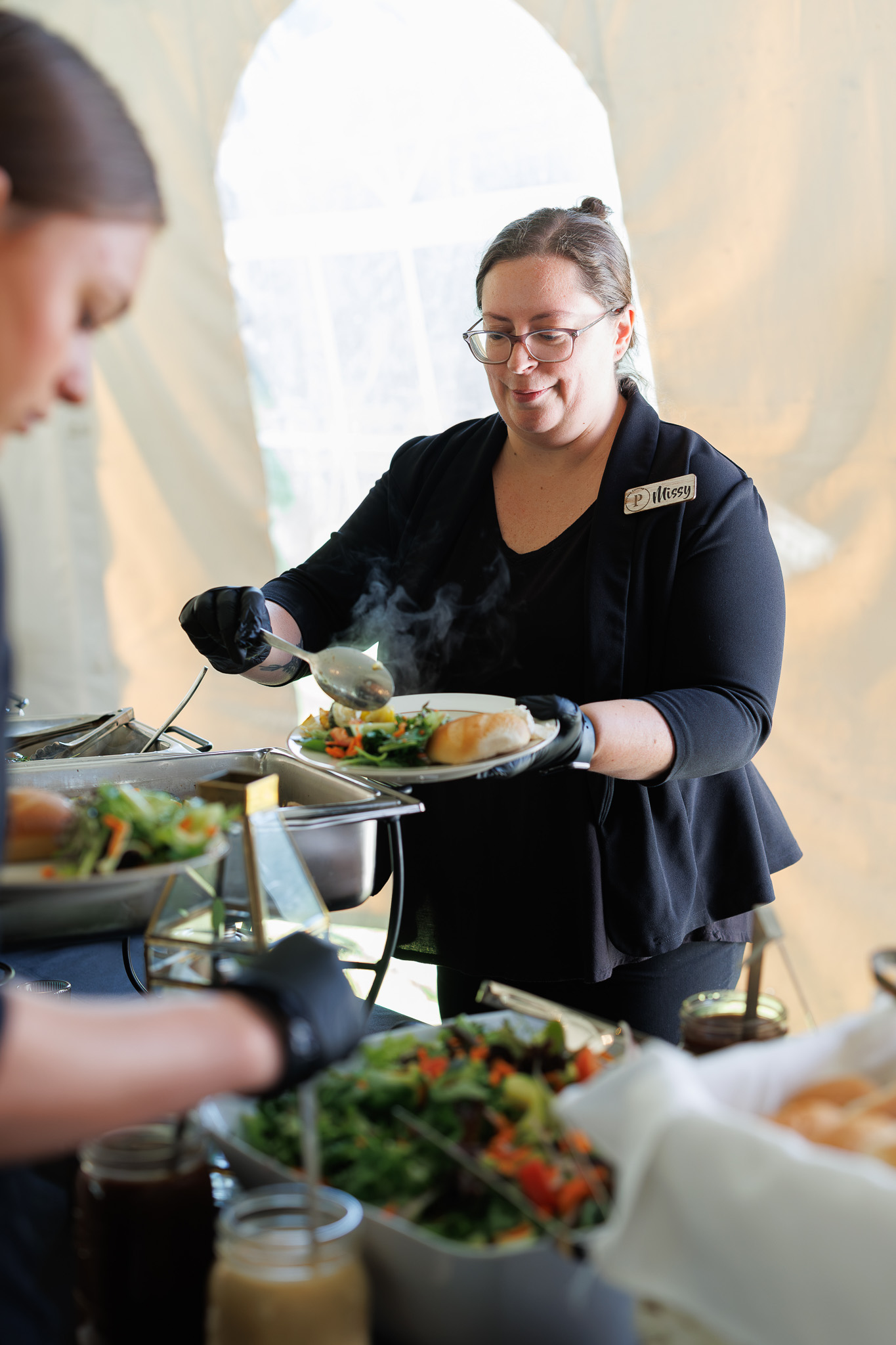 Partyman Catering Wedding Buffet Service Partyman Catering team member serving a guest from a hot wedding buffet with fresh salad and dinner rolls.