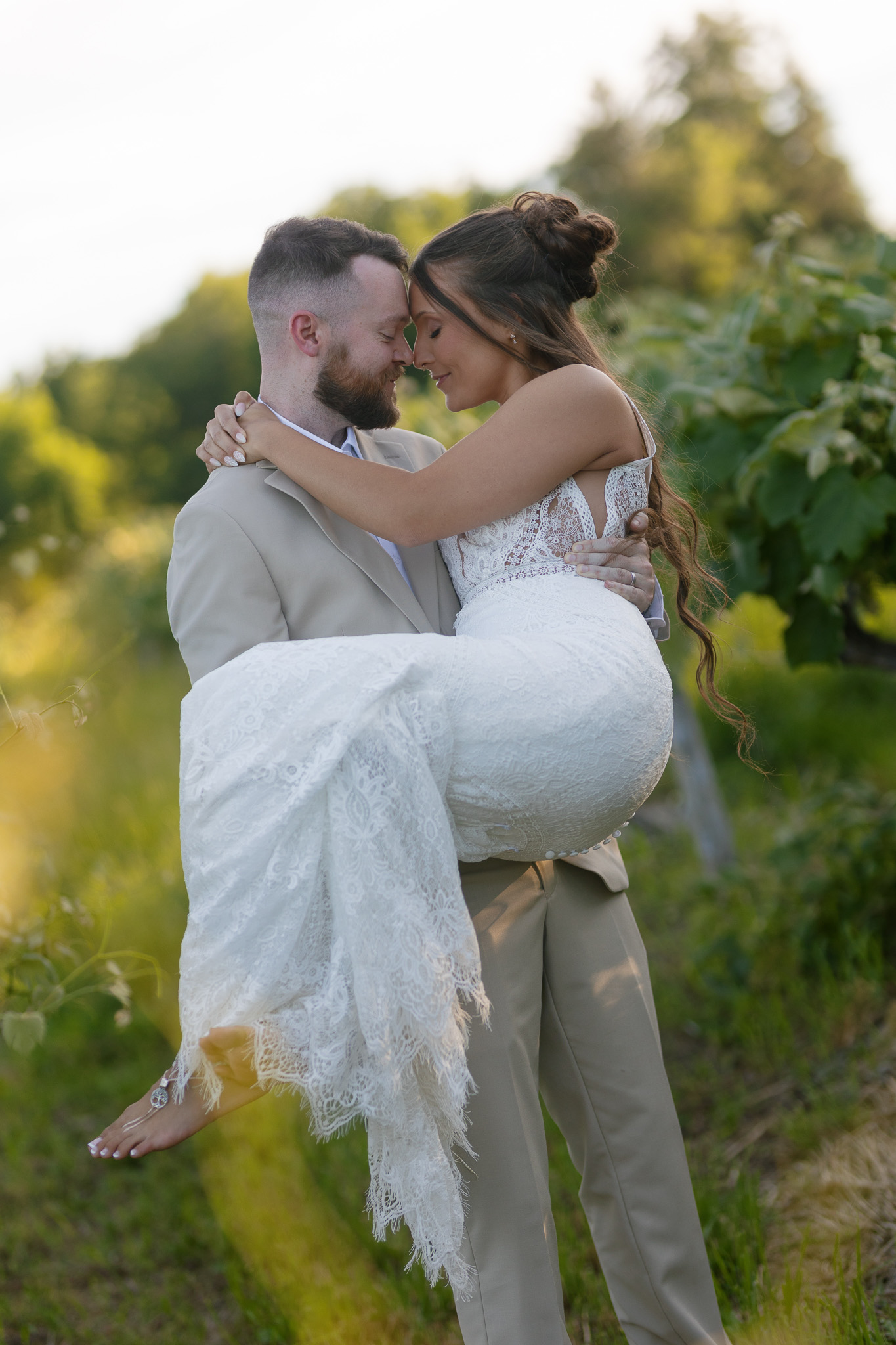 Romantic Bride and Groom Wedding Portrait in the Vineyard Groom holds his bride in a romantic outdoor wedding portrait surrounded by lush greenery and vineyard vines.