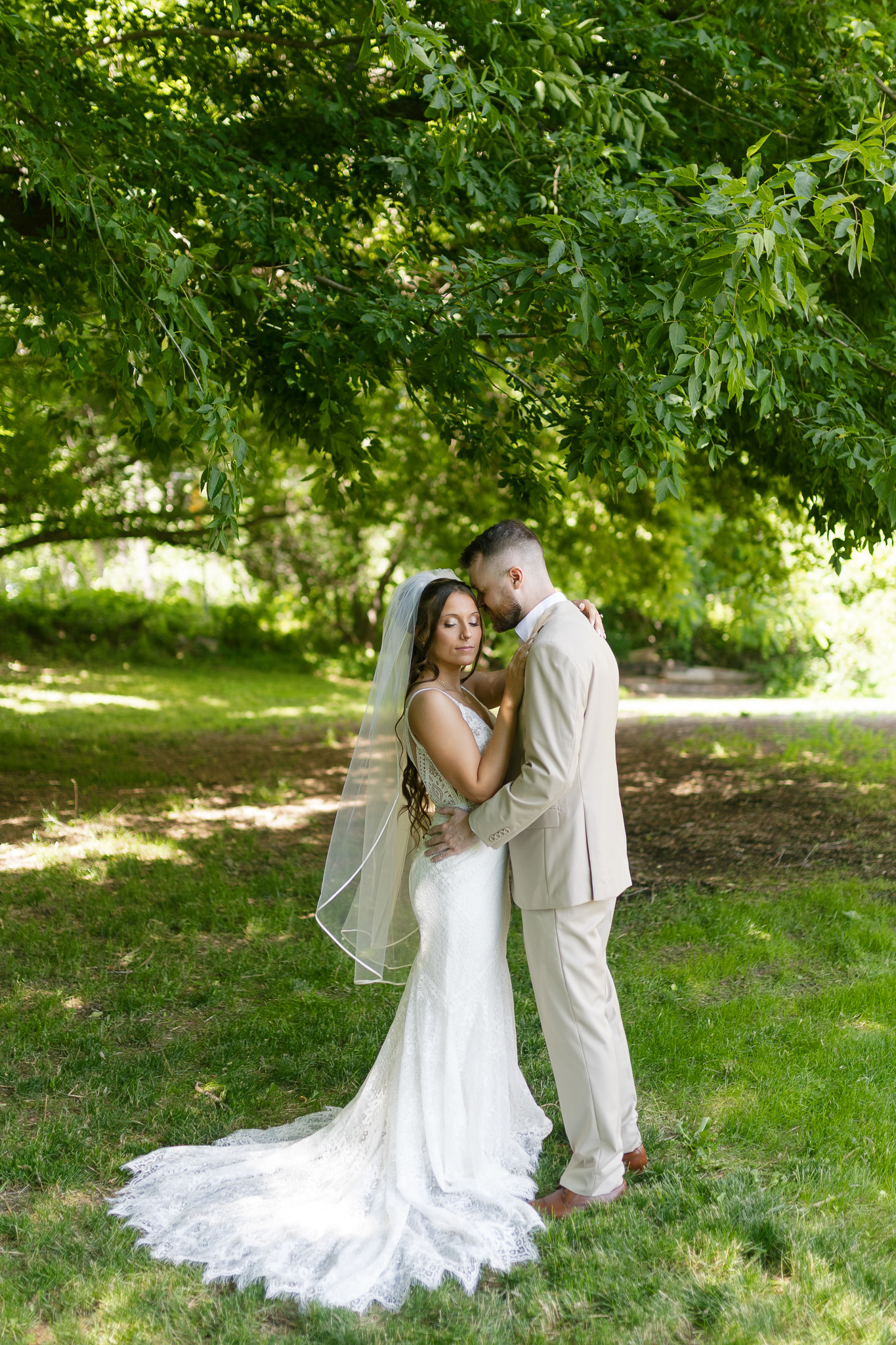 Romantic Outdoor Bride and Groom Portrait Bride and groom embracing beneath mature trees during their summer outdoor wedding portraits.