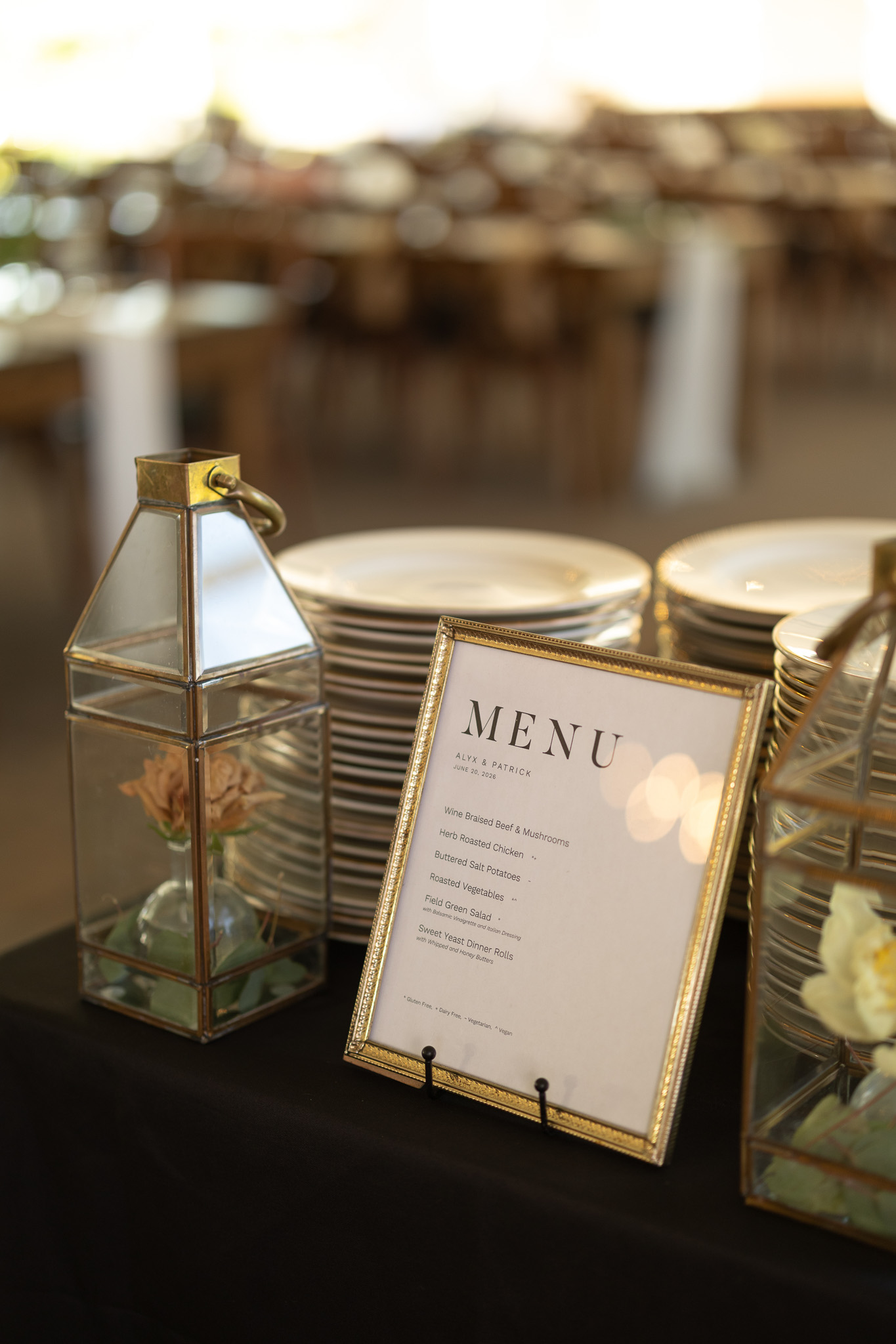 Inspire Moore – 6.20.26 – Partyman Framed wedding dinner menu displayed beside stacked plates, glass lanterns and floral accents at the buffet station.