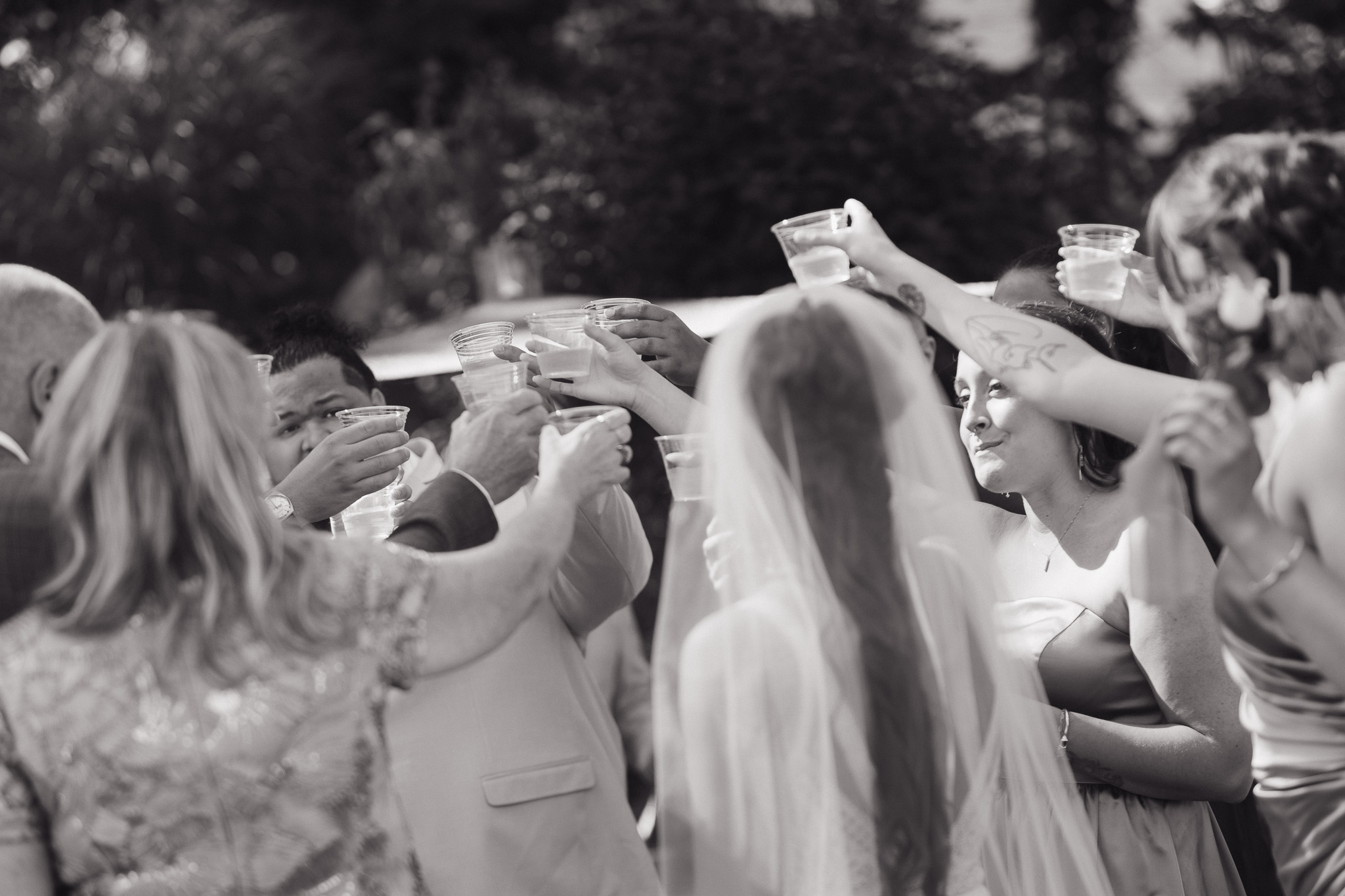Wedding Celebration Toast | Inspire Moore Winery Wedding Black-and-white candid photo of a bride surrounded by wedding guests raising their glasses for a celebratory toast at Inspire Moore Winery & Vineyard.