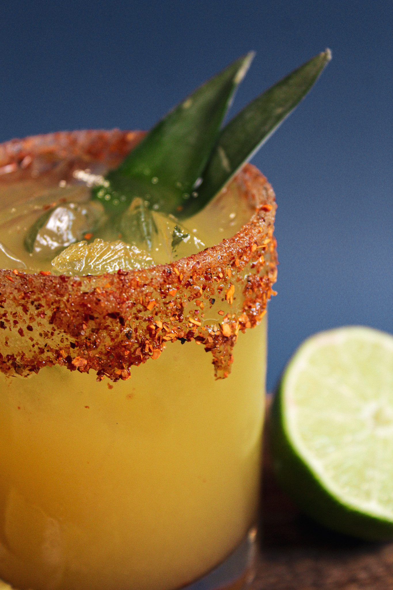 Spicy Pineapple Signature Cocktail by Partyman Catering Golden pineapple cocktail served over ice with a chili-spiced rim, fresh pineapple leaves, and lime.